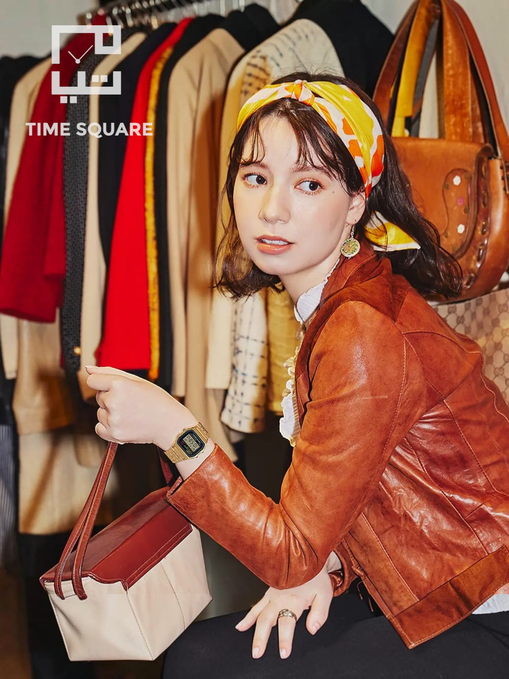 A woman wearing a brown leather jacket and a yellow patterned headscarf holds a beige and brown handbag in a boutique setting with clothing racks in the background. The TIME SQUARE logo is visible in the top left.