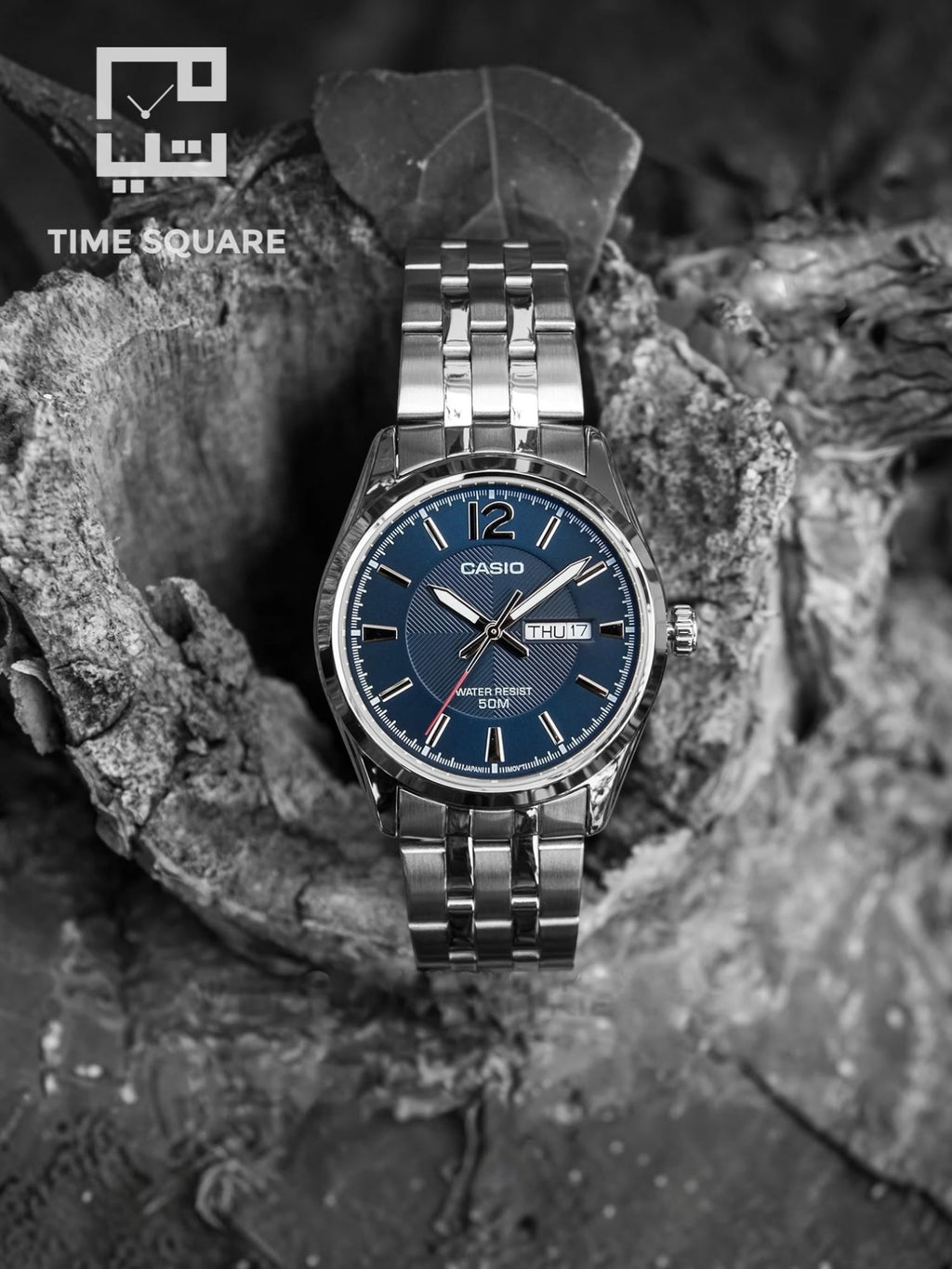 A Casio men's watch with a blue dial and silver stainless steel case and bracelet, displayed on a textured rock surface. The image is in black and white, with a 'TIME SQUARE' logo watermark in the top left corner.