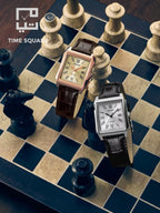 Two square analog wristwatches with dark brown leather straps are displayed on a chessboard. One watch has a rose gold-toned case and a beige dial, while the other has a silver-toned case and a white dial.