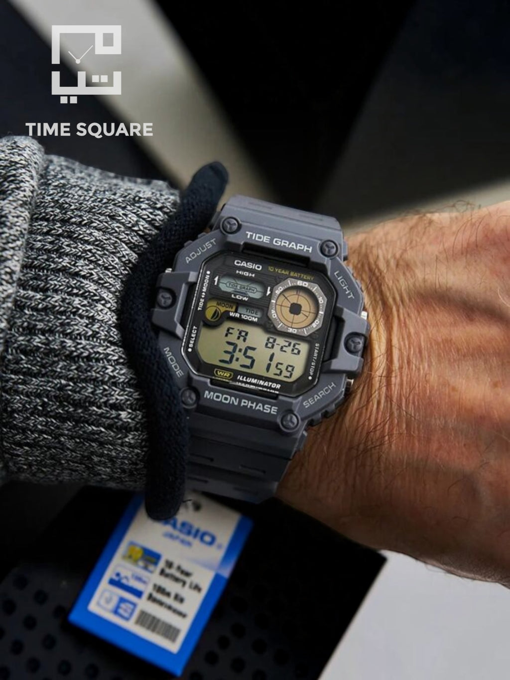 A close-up of a Casio digital watch with a dark gray rugged case and black strap, worn on a person's wrist. The watch face shows digital time.