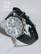 A Casio watch with a silver-toned stainless steel case, a white dial, and a black leather strap, resting on a light gray stone surface. The TIME SQUARE logo is visible in the top-left corner.